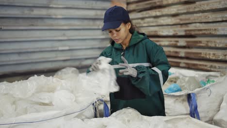 y una mujer afroamericana con un uniforme especial clasifica polietileno en una planta de reciclaje de residuos.