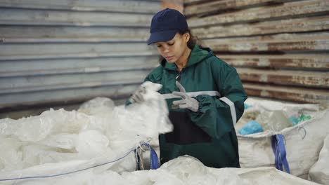 and african-american woman in a special uniform sorts polyethylene at a waste recycling plant. processing of raw materials