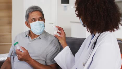 Mixed-race-female-doctor-and-senior-man-wearing-masks-and-holding-pills