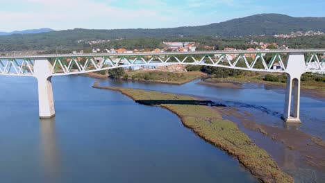 puente ferroviario sobre el río ulla, el pueblo y los edificios industriales y las montañas boscosas en el soleado cielo azul orizonte, drone derribado, catoira, galicia, españa