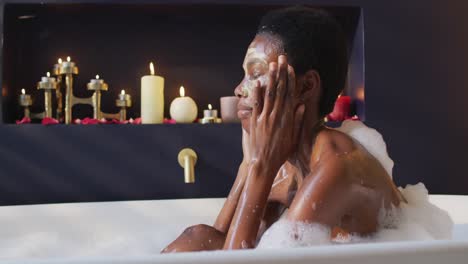 african american woman with towel and mask taking bath in bathroom