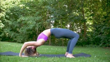 Woman-doing-yoga-outside-on-cool-green-grass-with-a-gentle-breeze-and-sunshine-moves-into-upward-bow-or-wheel-pose