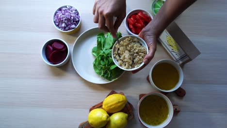 Luftaufnahme-Der-Zugabe-Von-Quinoa-Zu-Einem-Teller-Spinatsalat,-Zubereitung-Eines-Salats-Mit-Tomaten,-Karotten,-Spinat,-Kichererbsen,-Zitronen,-Zwiebeln,-Nüssen,-Dressing-Im-Blick