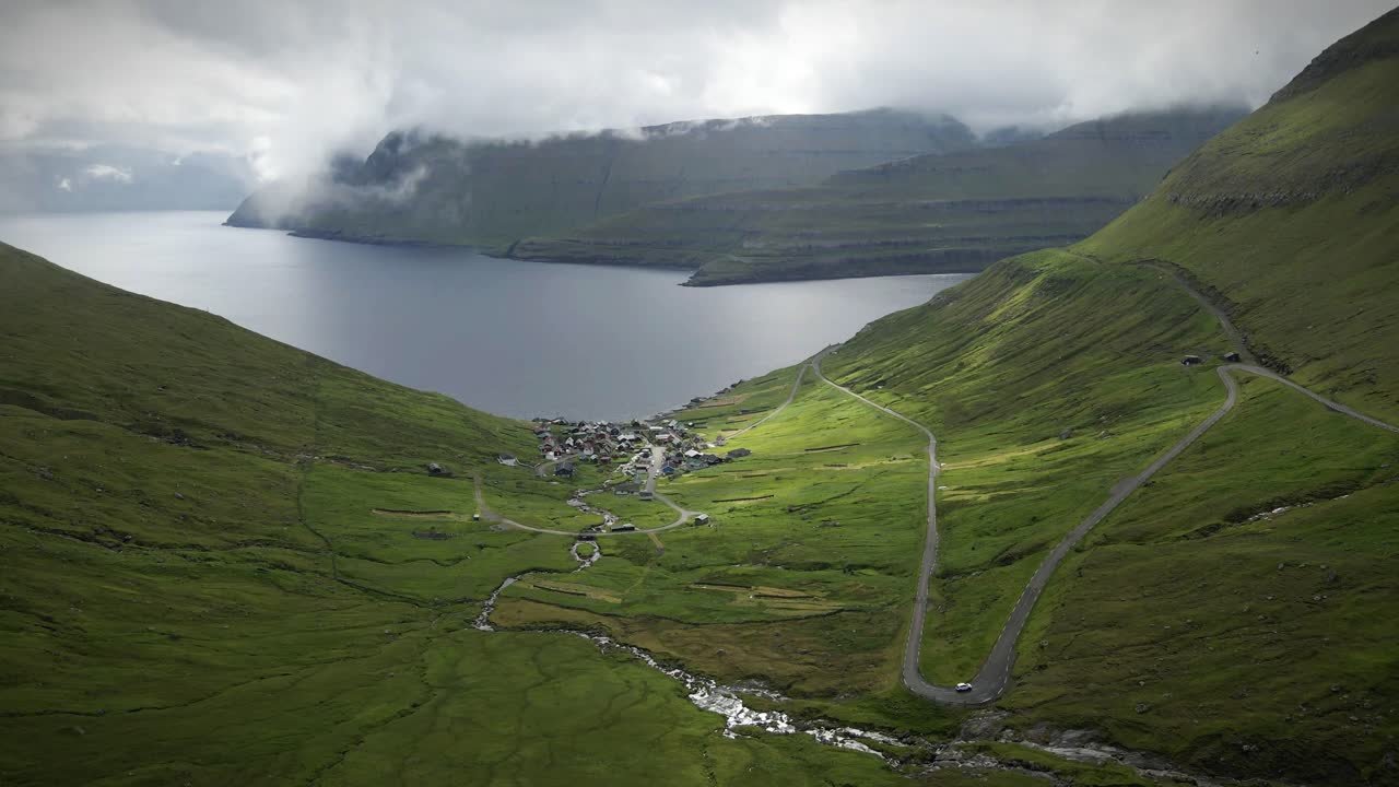 페로 제도의 닝스 (funnings) 에 있는 경치 좋은 계곡으로, 푸른 언덕, 휘어지는 도로, 작은 마을, 그리고 극적인 산 풍경으로 둘러싸인 평온한 바다 입구가 있습니다.