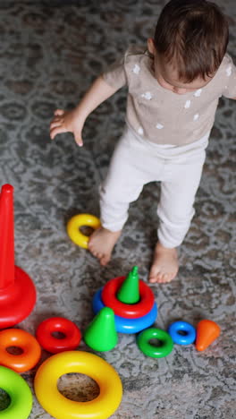 adorable caucasian boy assembling toy pyramids. kid plays on the carpet at home. view from top. vertical video