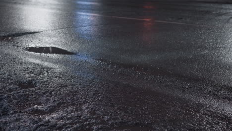 close-up view of a wet road at night, showcasing light reflections on the glistening surface as a car drives by