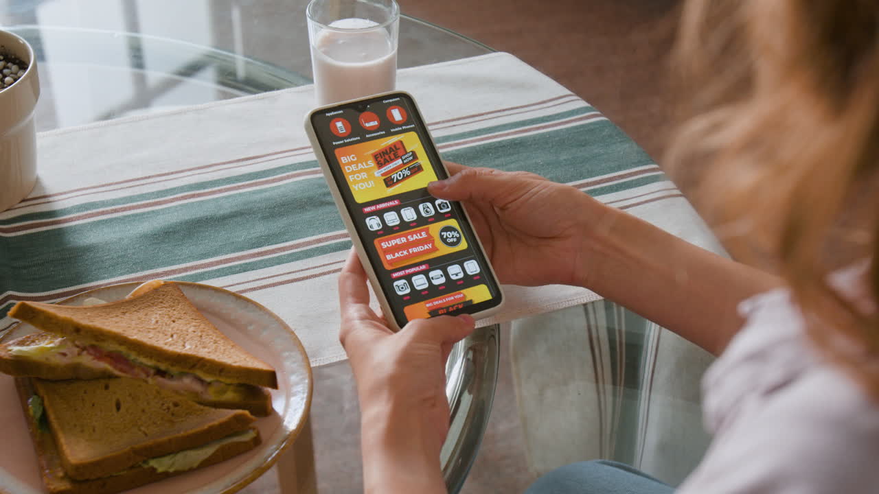 Person using retail app on smartphone with sandwich and milk nearby