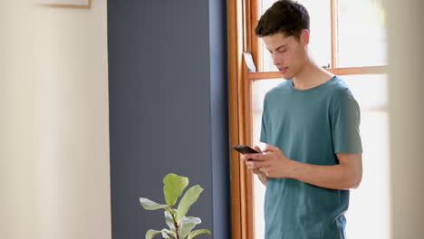 Happy-biracial-man-using-smartphone-standing-in-sunny-living-room,-copy-space,-slow-motion