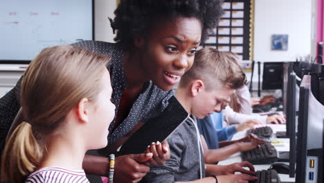 teacher helping female pupil in line of high school students working at screens in computer class