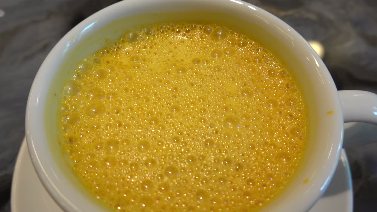 Close up of a yellow beverage in a white cup on a marble table