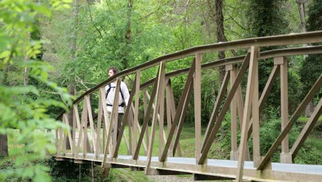 Outdoors-shot-of-a-man-hiking-over-a-small-bridge-on-a-nature-trail-in-Catalonia-Spain