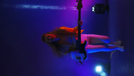 vertical video crazy women rock musician playing guitar in the studio in the light of spotlights and smoke dancing and jumping in the studio