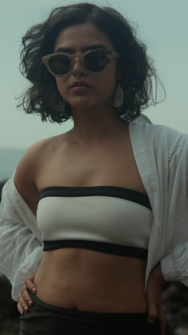 Close-up of a woman in sunglasses and bandeau top, posing confidently by the coast