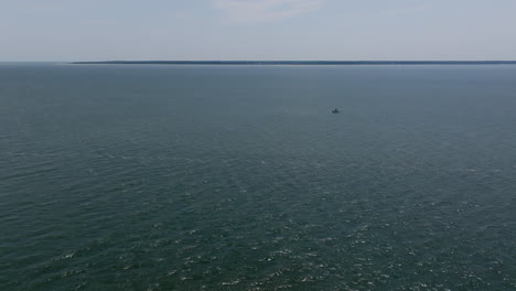 a single boat floats peacefully on calm, open water, far from shore under a bright sky, emphasizing the stillness of the surrounding sea