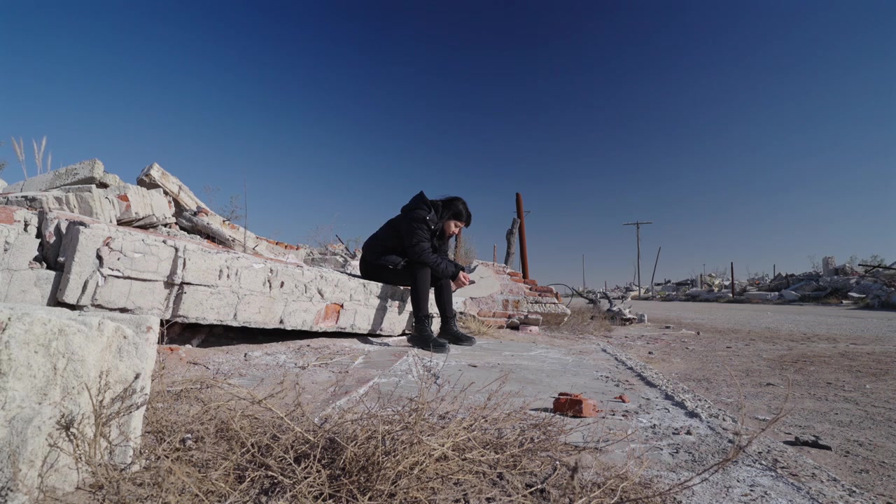 Donna sola e pensierosa seduta su strutture di cemento in rovina a Villa Epecuen, Adolfo Alsina, Provincia di Buenos Aires, Argentina, tra i depositi salini lasciati dall'alluvione, inquadratura statica a livello del suolo, resilienza.