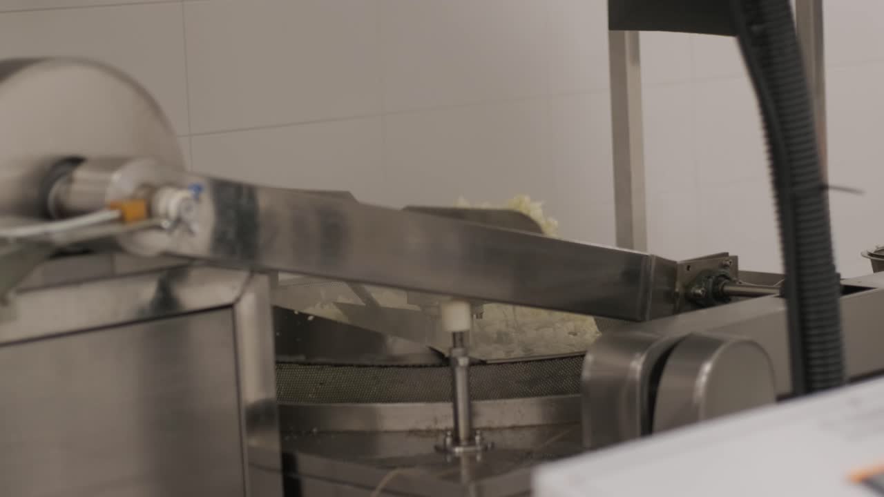 Production of potato chips and snacks. Industrial deep frying machine. Chips are fried in a large bowl with oil. Production factory line moves golden potato chips after frying.