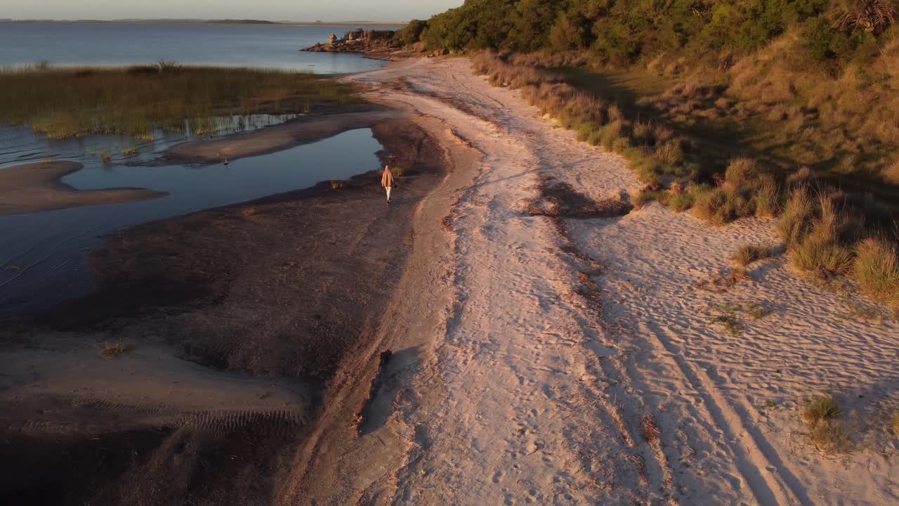 toma cinematográfica hacia atrás de una persona caminando por la orilla del lago en una hermosa puesta de sol cerca de la laguna negra en uruguay