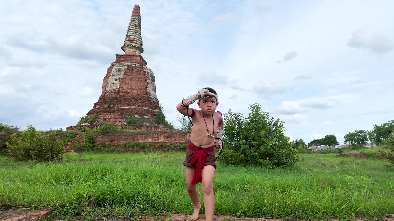 Đứa trẻ châu Á biểu diễn các động tác võ thuật truyền thống ngoài trời gần ngôi chùa đá cổ kính dưới ánh sáng ban ngày
