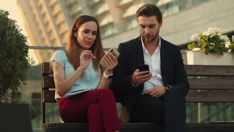 Confident-businessman-and-businesswoman-using-smartphones-in-modern-city