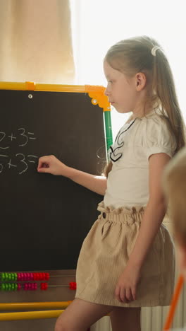 girl writes on blackboard with tiny piece of chalk and looks into empty hand. schoolgirl studies mathematics with brother. siblings do homework together