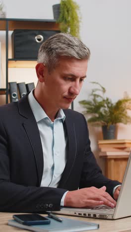 smiling young businessman in formal suit working on laptop computer sitting at desk in home office