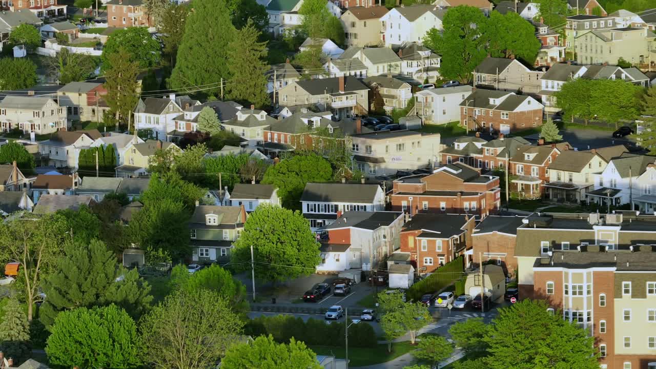 Row of houses in american neighborhood during golden peaceful sunset time. Aerial wide shot. Green trees in May. Car on street. Traditional homes in small city of Ephrata, PA.