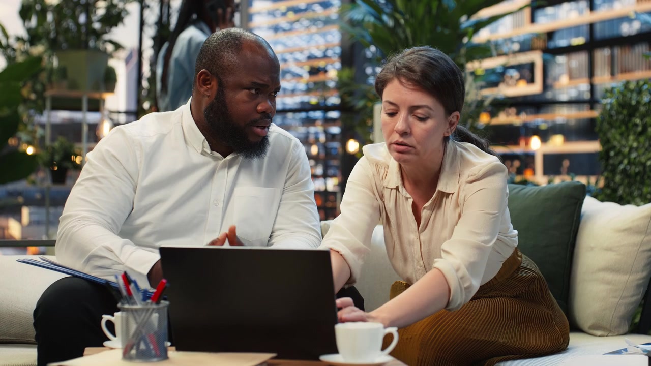 Coworkers collaborating on laptop presentation, sitting on city rooftop terrace