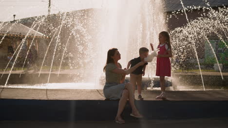 boy bites cotton candy with mother and sister near fountain