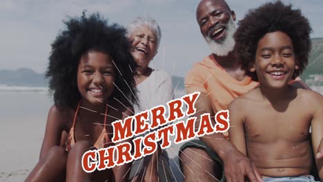 Animation-of-merry-christmas-over-happy-diverse-grandparents-and-grandchildren-on-beach