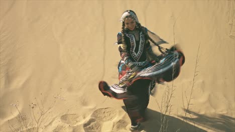 mujer gitana bailando en el desierto frente a una duna de arena