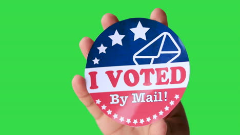 hand of a man holding i voted by mail sticker against green screen chroma key