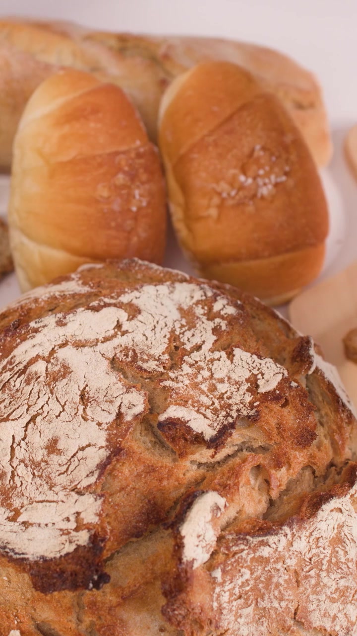 Close-up shot of hand selecting multigrain bread slice from variety of fresh artisan loaves.
