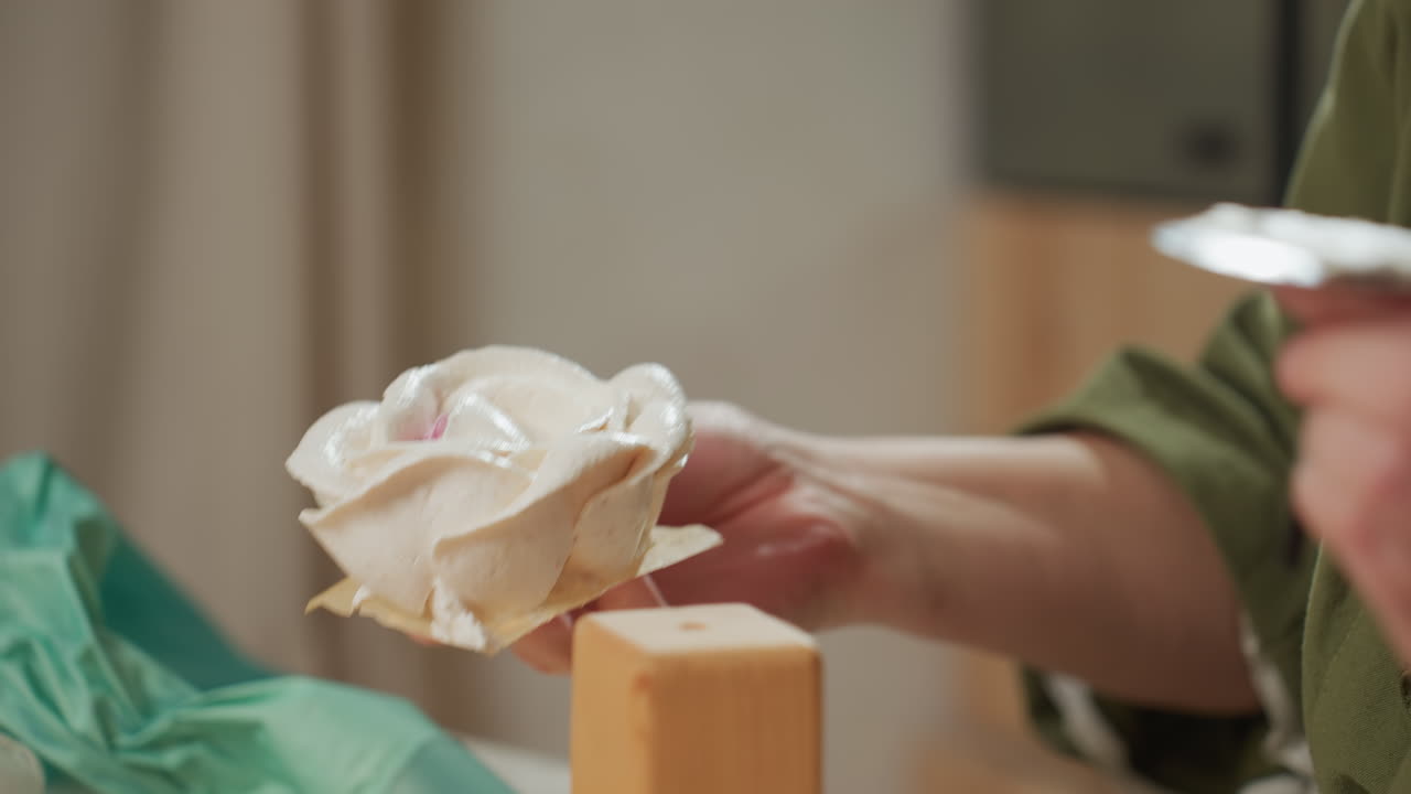 Close up of baker gently holding detailed flower-like icing cake, preparing to place it on table with other cupcakes, showcasing craftsmanship and precision of handmade dessert