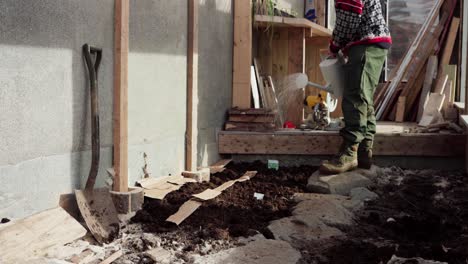 hombre rociando el suelo con semillas usando una olla de riego dentro del invernadero