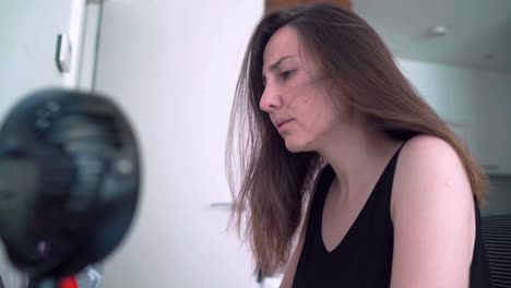 exhausted woman working with laptop computer cools off with breeze from a desk fan during a hot summer day