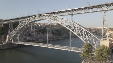 aerial drone view of iconic dom luís i bridge in porto, portugal, with double-deck iron arch spanning douro river, connecting porto and vila nova de gaia under clear blue sky in daylight