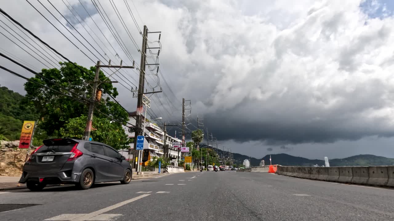 Low-angle view of cars and scooters passing under dramatic rain clouds on a Phuket roadside