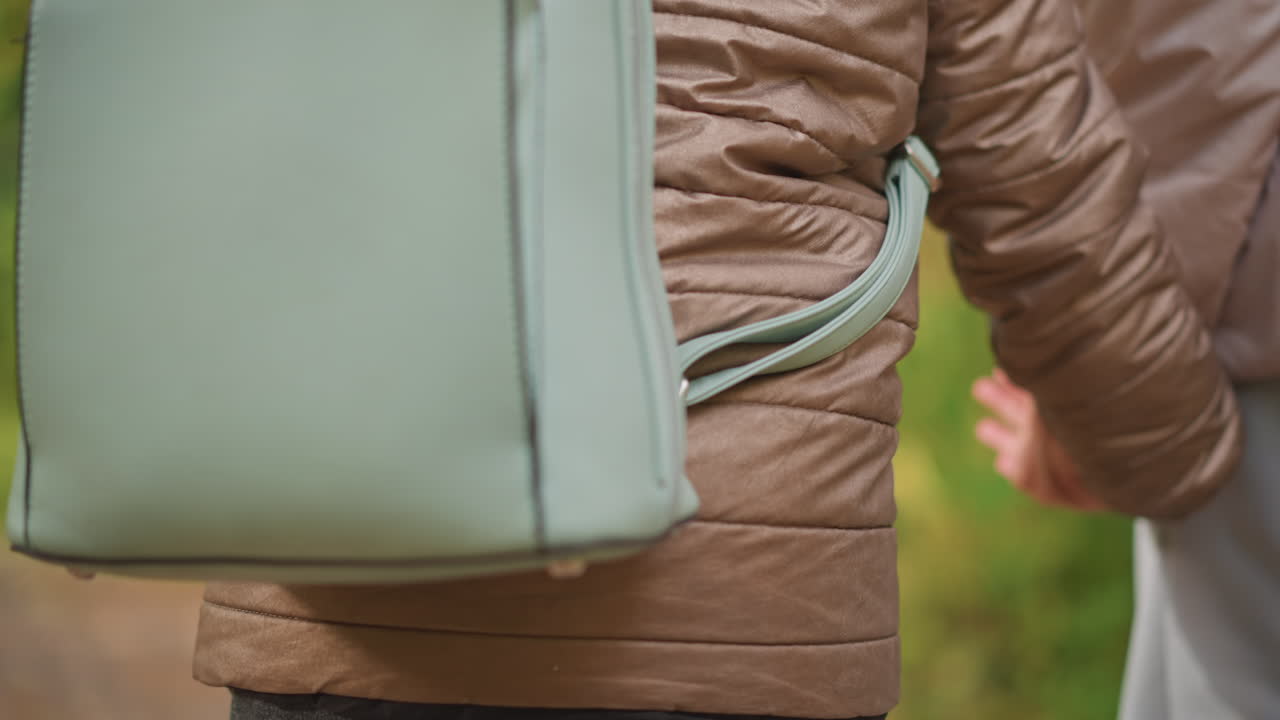 close rear view of child and adult wearing padded jackets walking side by side holding hands on forest trail, showing tender connection and calm moment in outdoor autumn environment