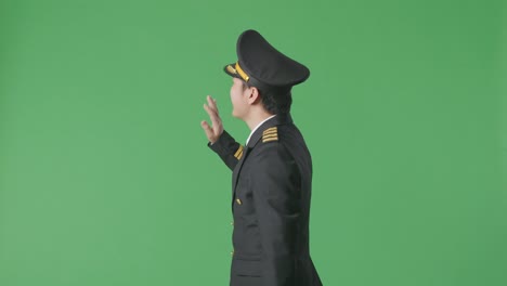 side view of asian man pilot walking and waving hand in the green screen background studio