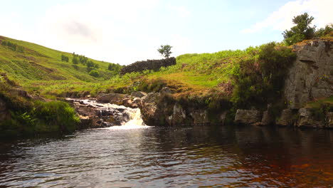 Static-shot-of-a-rock-pool-in-a-stream-being-filled-by-a-waterfall,-bright-sunny-day