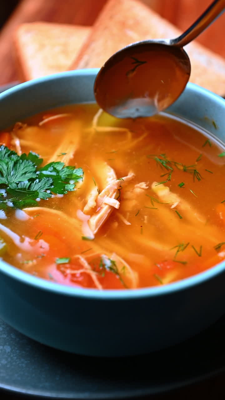 Suppe med ske og grøntsagsblanding. Klar orange suppe med krydderurter, grøntsager og en ske i skålen