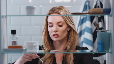 view through bathroom cabinet of young businesswoman cleaning ears with cotton wool buds