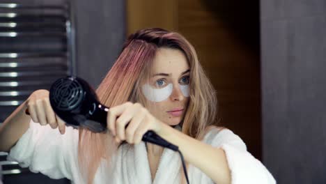 Woman-in-bathroom-mirror-and-drying-her-hair-with-hair-dryer-and-brush