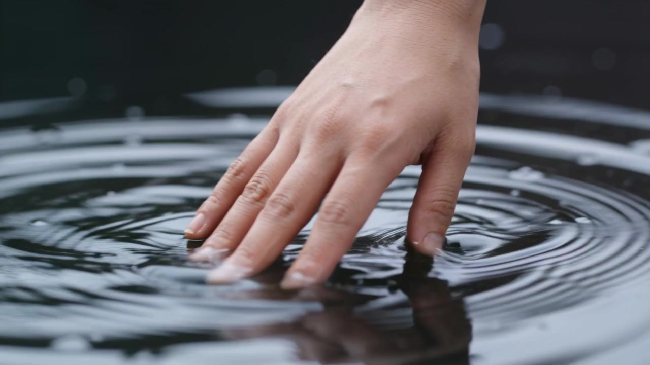 Touching right fingertips pressing into basin water, creating ripples, droplets and reflection