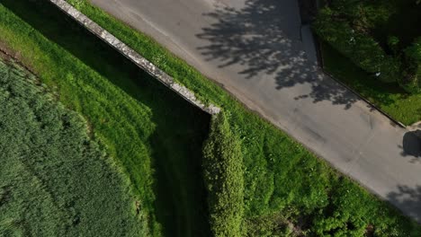 caledon border wall, county tyrone, northern ireland, may 2023. drone ascending twist, border wall, rural road and vibrant green fields, historic landscape aerial view on sunny day.