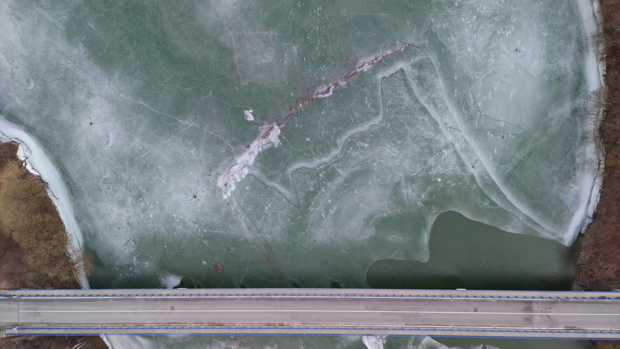 In the Košice Region of Slovakia, the frozen Ružín reservoir near Malý Folkmar shows icy patterns over the local bridge amid surrounding forest in a rural landscape captured from a drone.