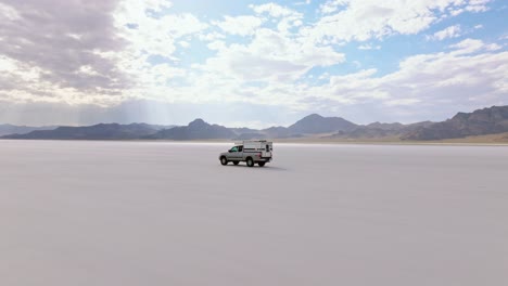 Car drives across serene Bonneville Salt Flats under cloudy sky