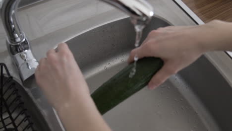 slow motion over the shoulder top view as a hand washing a cucumber over a sink in the kitchen