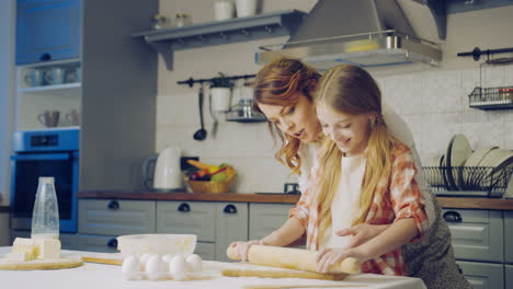 beautiful woman and her little daughter making a daugh for the cookies on the kitchen table in the evening. indoors