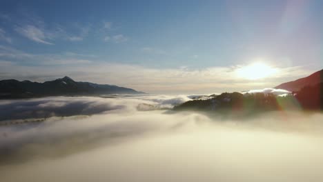 Drone-shot-of-an-incredible-landscape-covered-under-the-fog-with-surrounding-mountains-in-the-morning-at-winter-time-in-Slovenia-captured-in-4k,-drone-going-backward